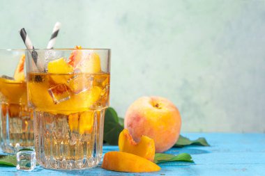 Homemade peach ice tea with ripe fresh peaches on high-colored blue wooden background