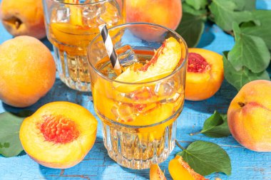Homemade peach ice tea with ripe fresh peaches on high-colored blue wooden background