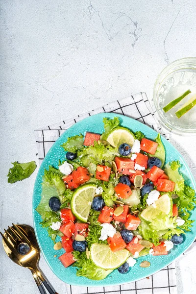 Summer watermelon salad. Fresh raw green salad with lettuce, arugula, watermelon slices, blueberry, feta cheese and honey