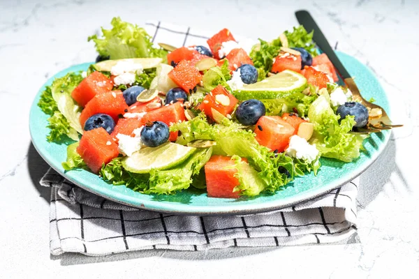 Summer watermelon salad. Fresh raw green salad with lettuce, arugula, watermelon slices, blueberry, feta cheese and honey