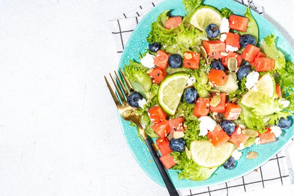 Summer watermelon salad. Fresh raw green salad with lettuce, arugula, watermelon slices, blueberry, feta cheese and honey