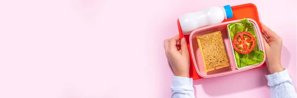 Healthy school meal, back to school concept. Children packed lunch box with balanced diet snack food - yogurt, cereal toast sandwich, apple, fresh vegetable salad, high-colored bright background