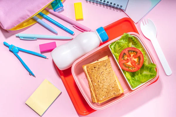 Healthy school meal, back to school concept. Children packed lunch box with balanced diet snack food - yogurt, cereal toast sandwich, apple, fresh vegetable salad, high-colored bright background