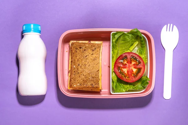 Healthy school meal, back to school concept. Children packed lunch box with balanced diet snack food - yogurt, cereal toast sandwich, apple, fresh vegetable salad, high-colored bright background