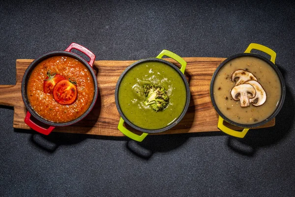 Autumn vegetable cream soups set. Three portion pots with various vegan hot vegetable cream soups tomato, mushrooms, broccoli on rustic wooden table copy space
