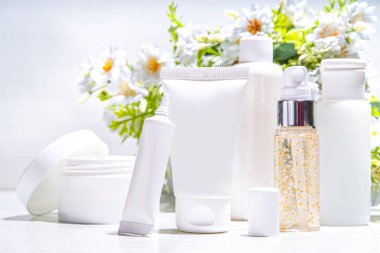 Aranan ve vahşi hasat edilmiş güzellik, kozmetik cilt ürünleri beyaz arka planda yabani çiçeklerle birlikte. Beyaz kavanozları, tüpleri, damlatıcıları, şişeleri ayarlayın. Spa, günlük organik doğal cilt bakımı.