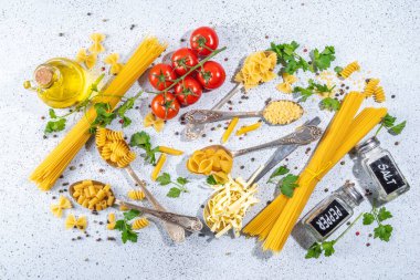 Beyaz masa arkasında çeşitli kurutulmuş spagetti, makarna ve kaşıklarla hazırlanmış makarna. Farklı şekillerde çiğ İtalyan makarnası, otlar, zeytinyağı, domatesler, baharatlar.