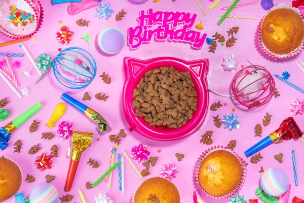 Pet cat happy birthday background with set different cats and kitty snack, food and toys, cat muzzle shape bowl, birthday cupcakes with happy birthday candles, accessories. Flatlay on pink background