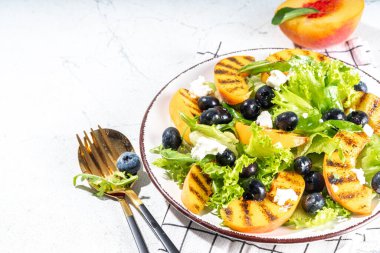 Summer peach salad. Fresh raw green salad with lettuce, arugula, grilled peach wedges, blueberry, feta cheese and honey