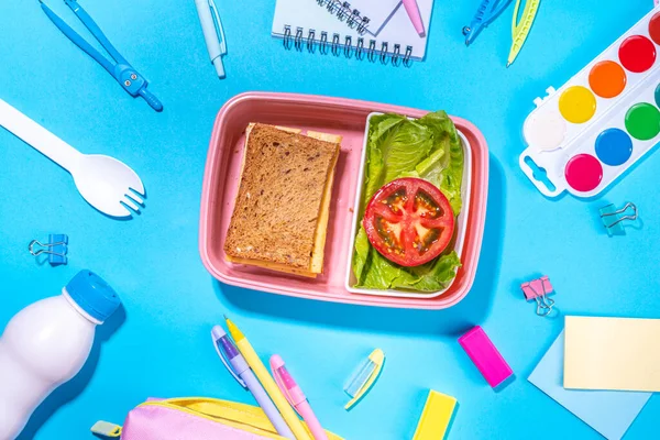 Healthy school meal, back to school concept. Children packed lunch box with balanced diet snack food - yogurt, cereal toast sandwich, apple, fresh vegetable salad, high-colored bright background