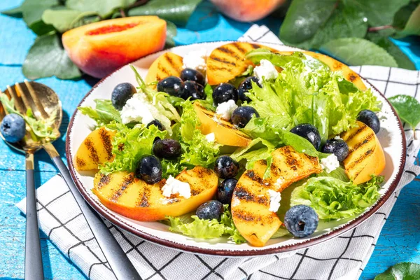Summer peach salad. Fresh raw green salad with lettuce, arugula, grilled peach wedges, blueberry, feta cheese and honey