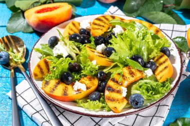 Summer peach salad. Fresh raw green salad with lettuce, arugula, grilled peach wedges, blueberry, feta cheese and honey