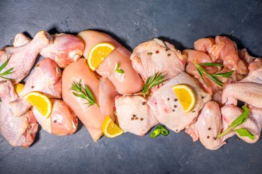 Çeşitli çiğ tavuk eti porsiyonları. Pişmemiş tavuk filetosu, but, kanatlar, şeritler ve bacaklar siyah yemek masasında baharatlı. 