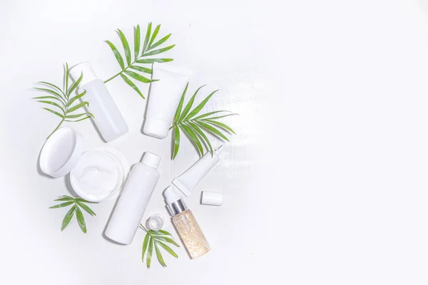 Beauty cosmetic skincare products on white background with tropical palm leaves flatlay copy space. Set of white jars, tubes, droppers and bottles. Summer spa, daily natural skin care routine concept