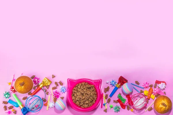 Pet cat happy birthday background with set different cats and kitty snack, food and toys, cat muzzle shape bowl, birthday cupcakes with happy birthday candles, accessories. Flatlay on pink background