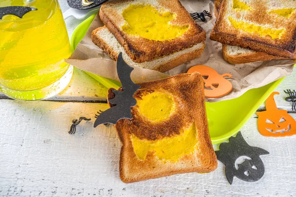 Funny food for kids, Halloween breakfast, lunch box: toast with scrambled eggs in the shape of Halloween monsters and ghosts, on wooden table with decorations, top view, copy space