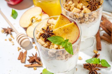 Apple Pie Granola Cheesecake, breakfast snack layered dessert with oat granola, cream cheese yogurt, honey, apple slices and cinnamon spices on white background copy space