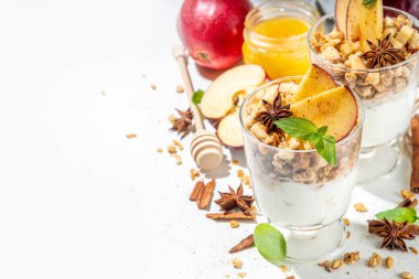 Apple Pie Granola Cheesecake, breakfast snack layered dessert with oat granola, cream cheese yogurt, honey, apple slices and cinnamon spices on white background copy space