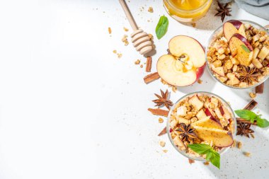 Apple Pie Granola Cheesecake, breakfast snack layered dessert with oat granola, cream cheese yogurt, honey, apple slices and cinnamon spices on white background copy space