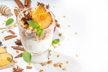 Apple Pie Granola Cheesecake, breakfast snack layered dessert with oat granola, cream cheese yogurt, honey, apple slices and cinnamon spices on white background copy space