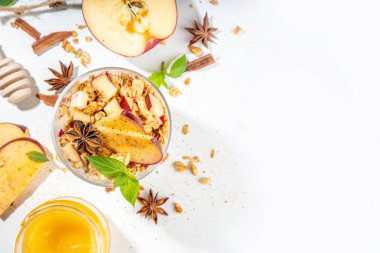 Apple Pie Granola Cheesecake, breakfast snack layered dessert with oat granola, cream cheese yogurt, honey, apple slices and cinnamon spices on white background copy space