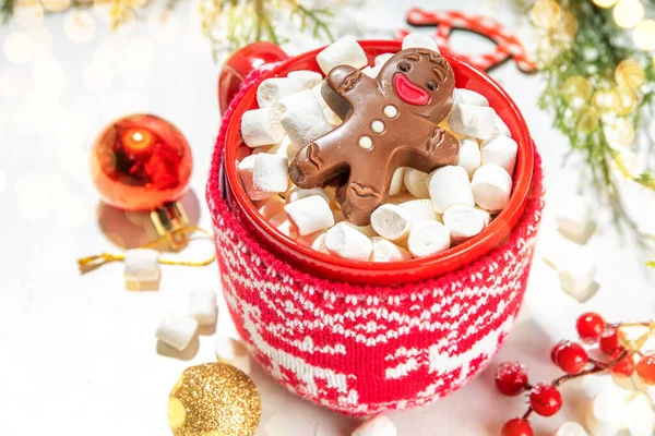 Christmas hot chocolate mug with funny cute gingerbread man made from chocolate, bathing playing in cocoa mug, with Christmas decorated white table. Xmas holiday greeting card background copy space