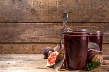 Red fig jam in small jar. Homemade autumn fig jam with fresh fruits. Fall preparations and canning on wooden table background copy space