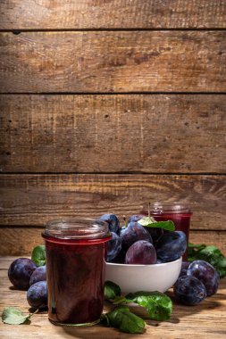 Red blue plum jam in small jar. Homemade autumn plum jam with fresh fruits. Fall preparations and canning on wooden table background copy space