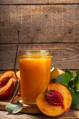 Red peach jam in small jar. Homemade autumn peach jam with fresh fruits. Fall preparations and canning on wooden table background copy space