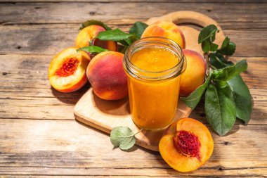 Red peach jam in small jar. Homemade autumn peach jam with fresh fruits. Fall preparations and canning on wooden table background copy space