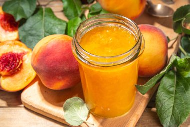 Red peach jam in small jar. Homemade autumn peach jam with fresh fruits. Fall preparations and canning on wooden table background copy space
