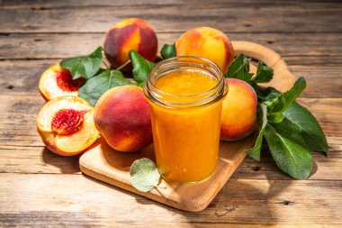 Red peach jam in small jar. Homemade autumn peach jam with fresh fruits. Fall preparations and canning on wooden table background copy space
