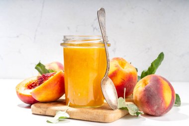 Peach jam in small jar. Homemade autumn peach jam with fresh fruits. Fall preparations and canning on white table background copy space