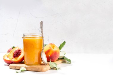 Peach jam in small jar. Homemade autumn peach jam with fresh fruits. Fall preparations and canning on white table background copy space