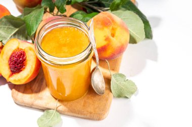 Peach jam in small jar. Homemade autumn peach jam with fresh fruits. Fall preparations and canning on white table background copy space