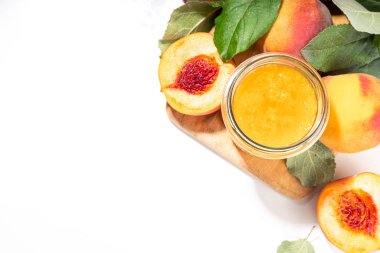 Peach jam in small jar. Homemade autumn peach jam with fresh fruits. Fall preparations and canning on white table background copy space