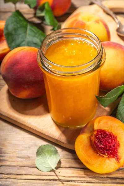 Red peach jam in small jar. Homemade autumn peach jam with fresh fruits. Fall preparations and canning on wooden table background copy space