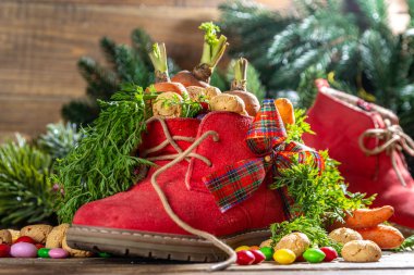 Sinterklaas, Saint Nicholas day background. Little kid red shoe with carrots and sweets, trooigoed, pepernoten, candy. Dutch Christmas holiday on cozy wooden background. 