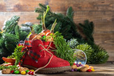 Sinterklaas, Saint Nicholas day background. Little kid red shoe with carrots and sweets, trooigoed, pepernoten, candy. Dutch Christmas holiday on cozy wooden background. 
