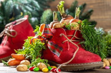 Sinterklaas, Saint Nicholas day background. Little kid red shoe with carrots and sweets, trooigoed, pepernoten, candy. Dutch Christmas holiday on cozy wooden background. 