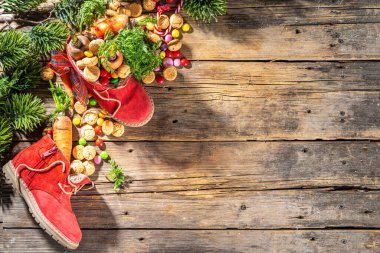 Sinterklaas, Saint Nicholas day background. Little kid red shoe with carrots and sweets, trooigoed, pepernoten, candy. Dutch Christmas holiday on cozy wooden background. 