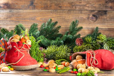 Sinterklaas, Saint Nicholas day background. Little kid red shoe with carrots and sweets, trooigoed, pepernoten, candy. Dutch Christmas holiday on cozy wooden background. 