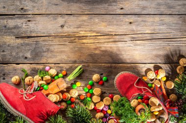 Sinterklaas, Saint Nicholas day background. Little kid red shoe with carrots and sweets, trooigoed, pepernoten, candy. Dutch Christmas holiday on cozy wooden background. 