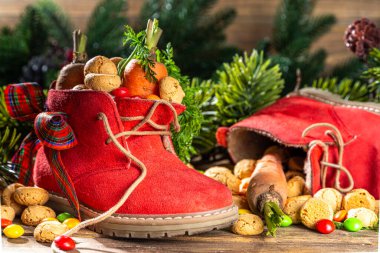 Sinterklaas, Saint Nicholas day background. Little kid red shoe with carrots and sweets, trooigoed, pepernoten, candy. Dutch Christmas holiday on cozy wooden background. 