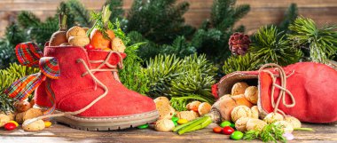Sinterklaas, Saint Nicholas day background. Little kid red shoe with carrots and sweets, trooigoed, pepernoten, candy. Dutch Christmas holiday on cozy wooden background. 