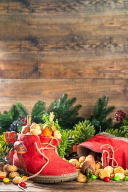 Sinterklaas, Saint Nicholas day background. Little kid red shoe with carrots and sweets, trooigoed, pepernoten, candy. Dutch Christmas holiday on cozy wooden background. 