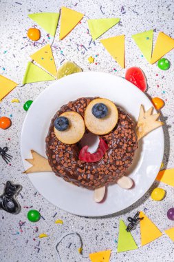 Fun Halloween Donuts. Creative decoration for chocolate donuts on Halloween  decorated table. Treat or trick holiday kid snack, white table background copy space