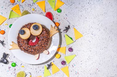 Fun Halloween Donuts. Creative decoration for chocolate donuts on Halloween  decorated table. Treat or trick holiday kid snack, white table background copy space