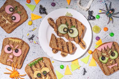 Funny halloween monster sandwiches. Set of various decorated monster sandwich and toasts, with cucumber, cheese and meat sausages, white table background with Halloween decorations