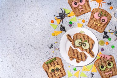 Funny halloween monster sandwiches. Set of various decorated monster sandwich and toasts, with cucumber, cheese and meat sausages, white table background with Halloween decorations